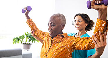 Senior woman lifting dumbbells, rehab tech assisting
