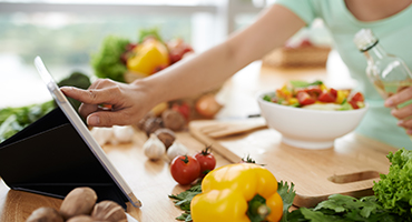 Closeup of hand touching computer tablet screen to advance recipe while chopping vegetables 