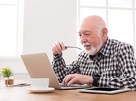 Un hombre sentado a la mesa de la cocina mirando una computadora portátil