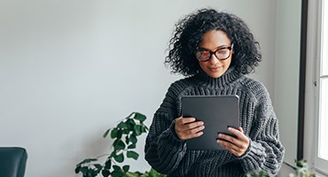 woman seated, watching programming on tablet computer