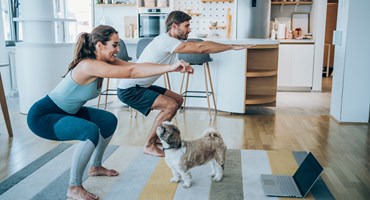 Couple doing squats in living room with dog