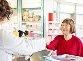 Mujer mayor con camisa roja pagando en una farmacia