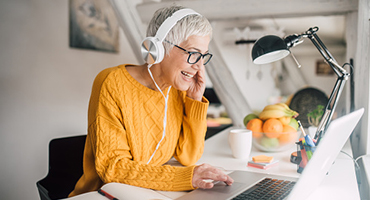senior woman in yellow shirt at computer with headphones