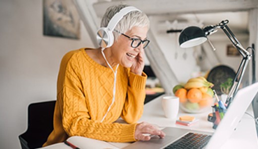 senior woman in yellow shirt at computer with headphones