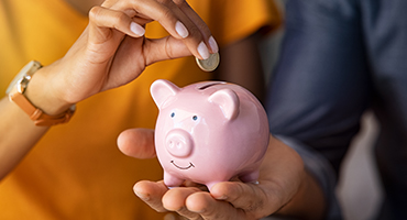 close up of couple putting coins into a piggy bank