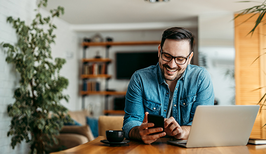 man viewing mobile phone and laptop from home office