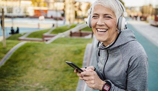 Mujer mayor feliz caminando al aire libre usando auriculares