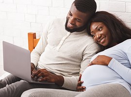 Healthy Expectations (Recursos para Embarazadas) Pareja relajándose sobre la cama y mirando una computadora portátil